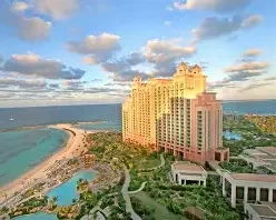 A large hotel building on the coast with a beach and ocean in the background, and a small pond and greenery in the foreground.