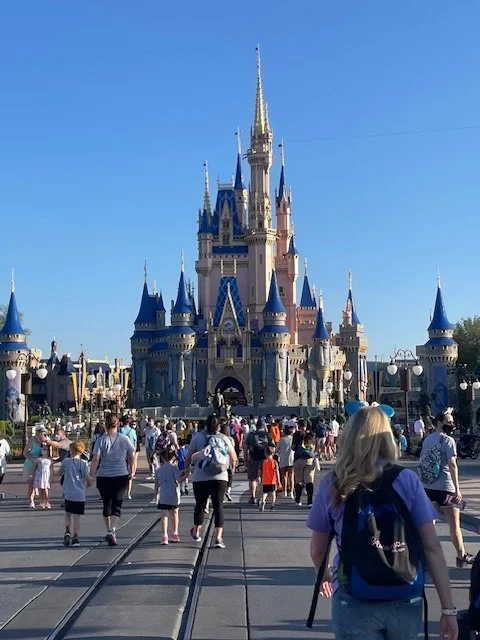 Disney castle at Disneyland with visitors walking towards it on a sunny day.