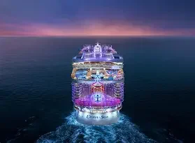 A brightly lit cruise ship sailing on the ocean at dusk with a colorful sky in the background.