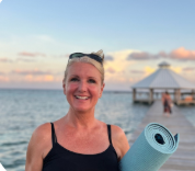 A smiling woman at the beach with a yoga mat over her shoulder