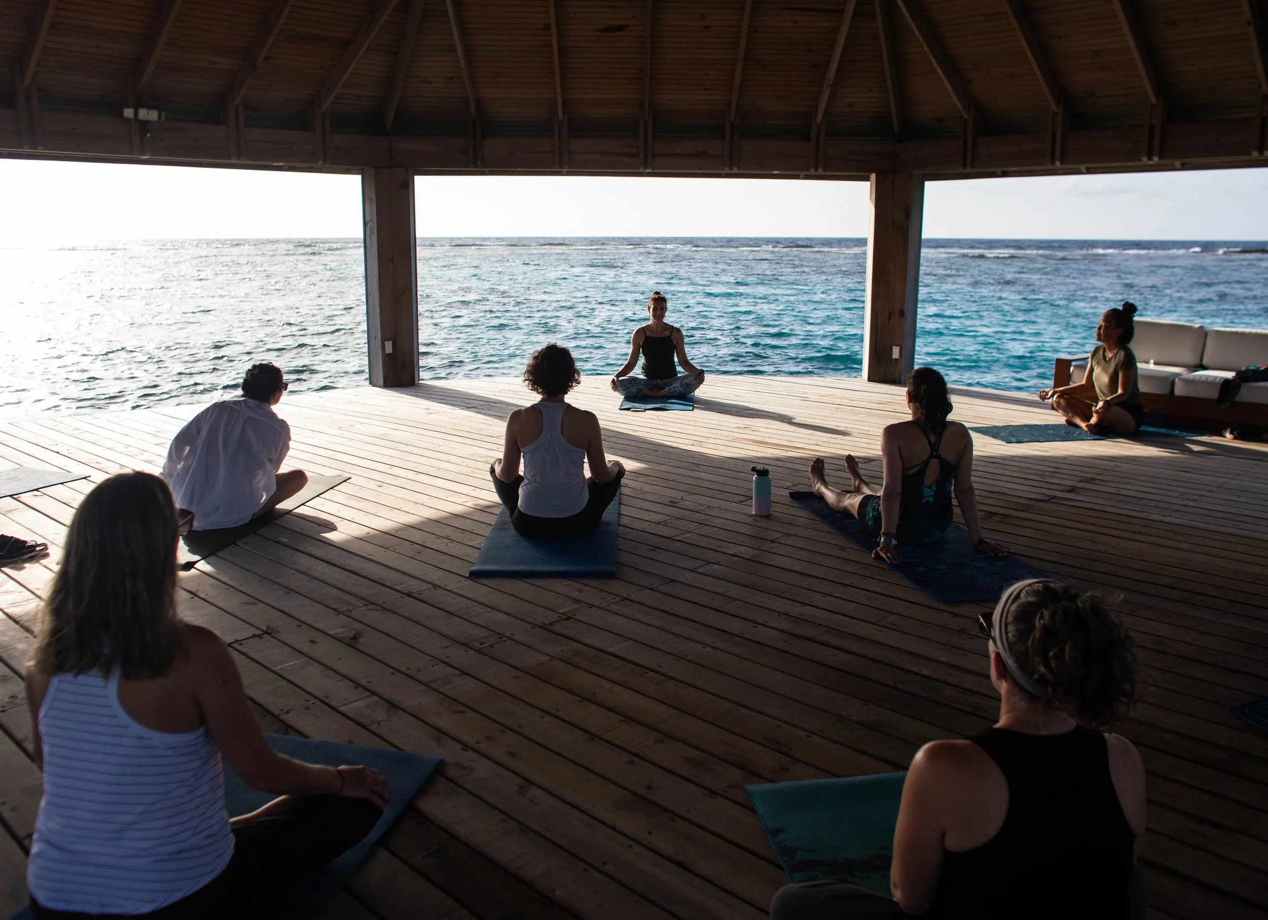 People practicing yoga on a wooden deck by the ocean during sunset.