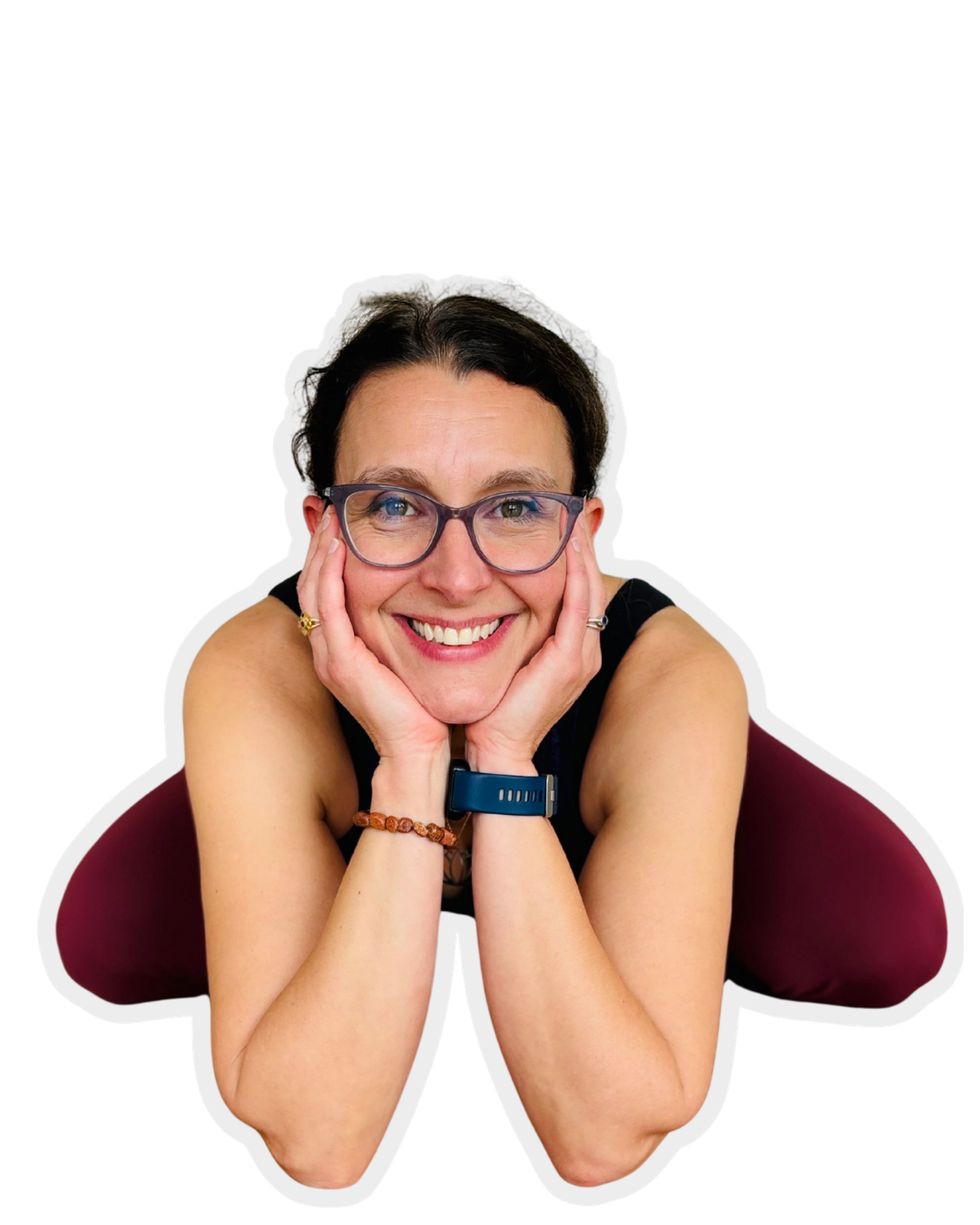 A woman with short dark hair, glasses, and a bright smile, resting her chin on her hands while leaning forward.