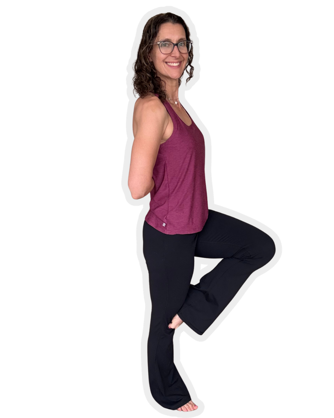 A woman with curly brown hair, wearing glasses, a purple sleeveless top, and black pants, is standing on one leg with the other knee raised and her hands behind her back, smiling at the camera.