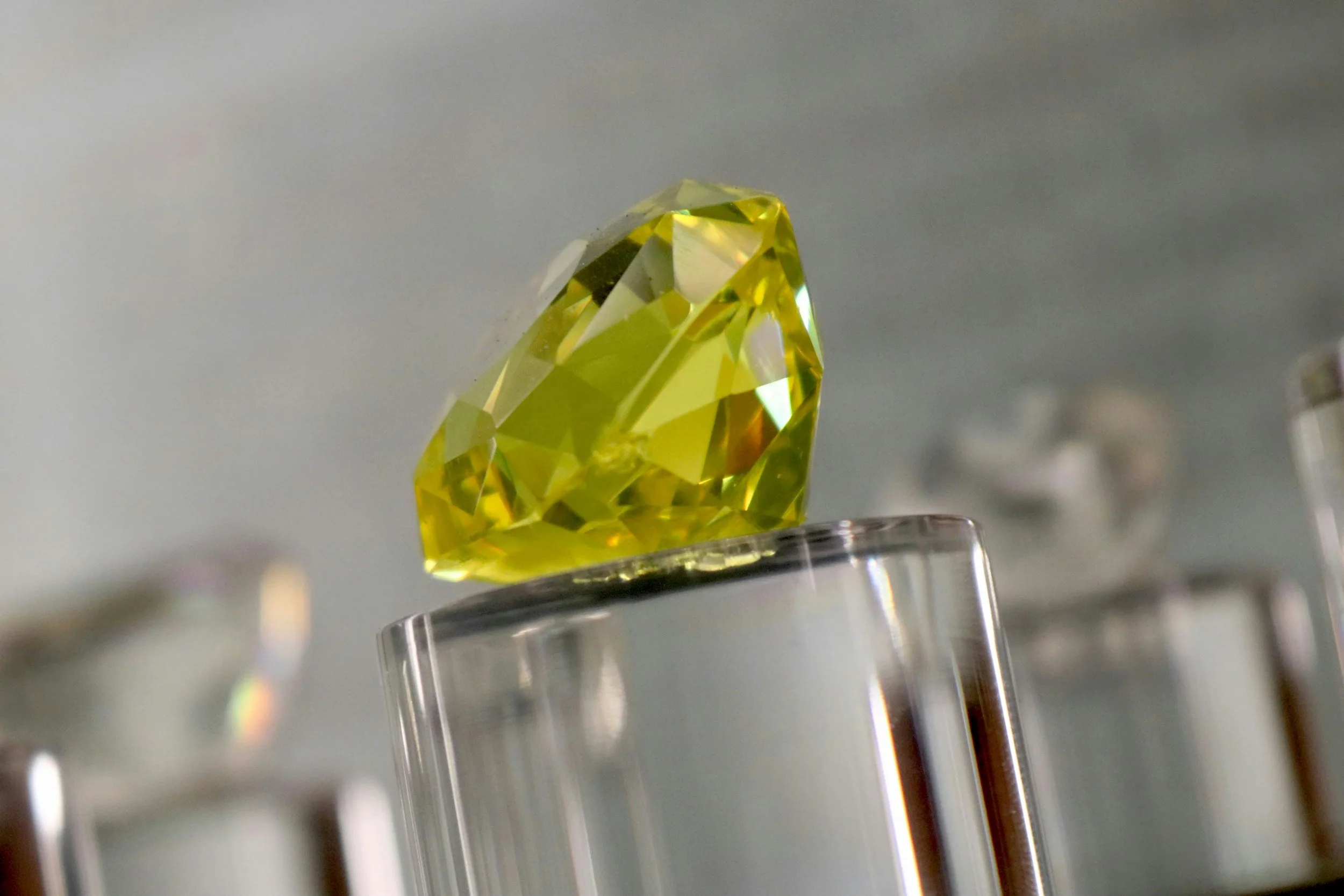 A yellow, faceted gemstone on a clear display stand.