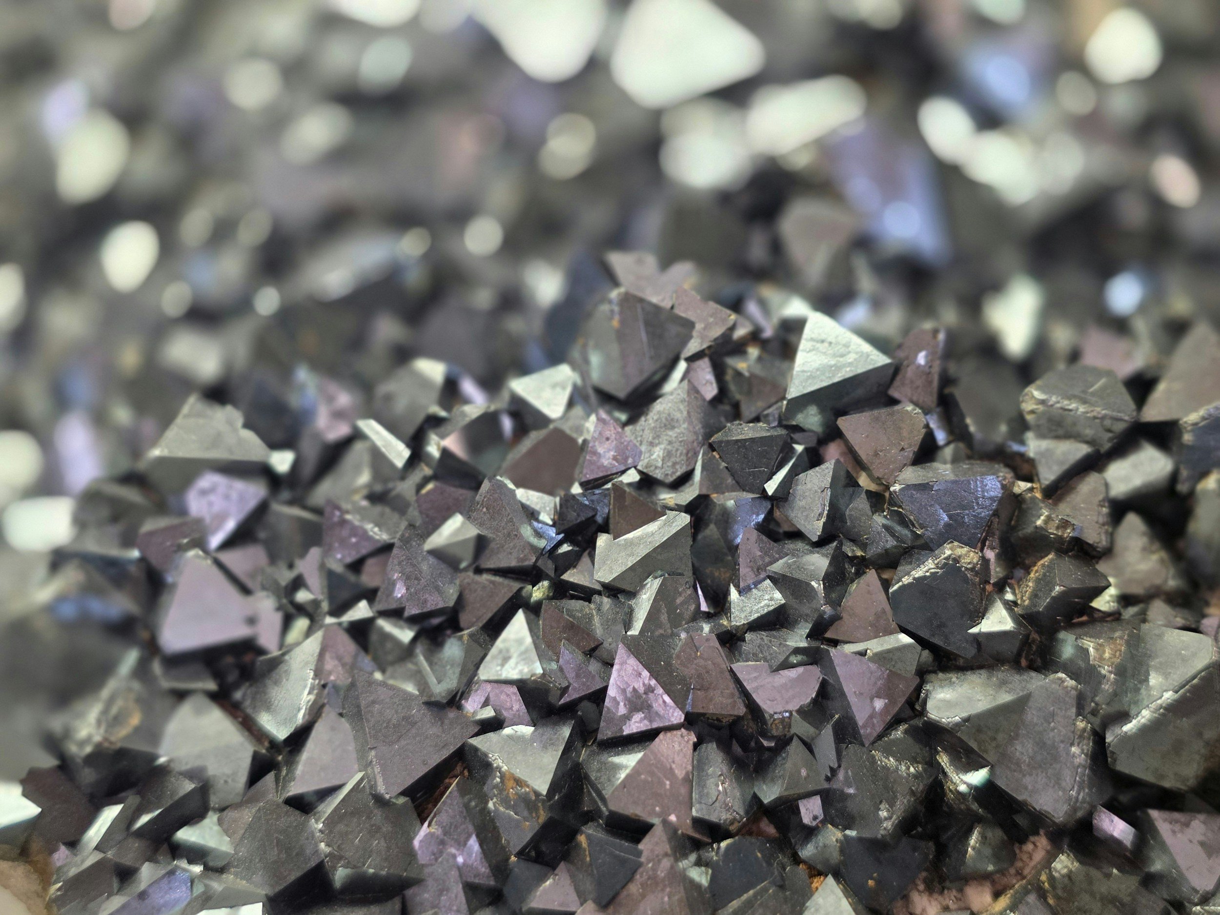 Close-up of metallic, iridescent, irregular-shaped crystals or mineral fragments with reflective surfaces and dark coloration.