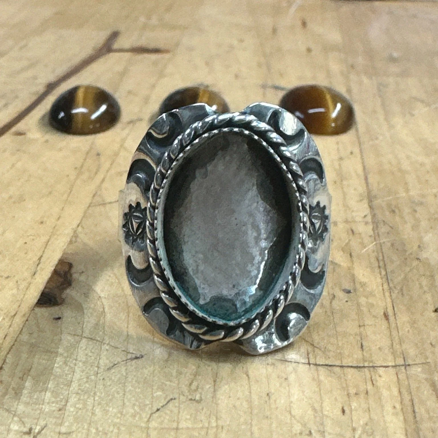 Three stones, one setting, one decision.
Commission Diaries, No. 1.

Someone asked for a tiger's eye shield ring. The setting got built first &mdash; crescents stamped around a twisted rope bezel, the whole blank shaped before any stone went near it.