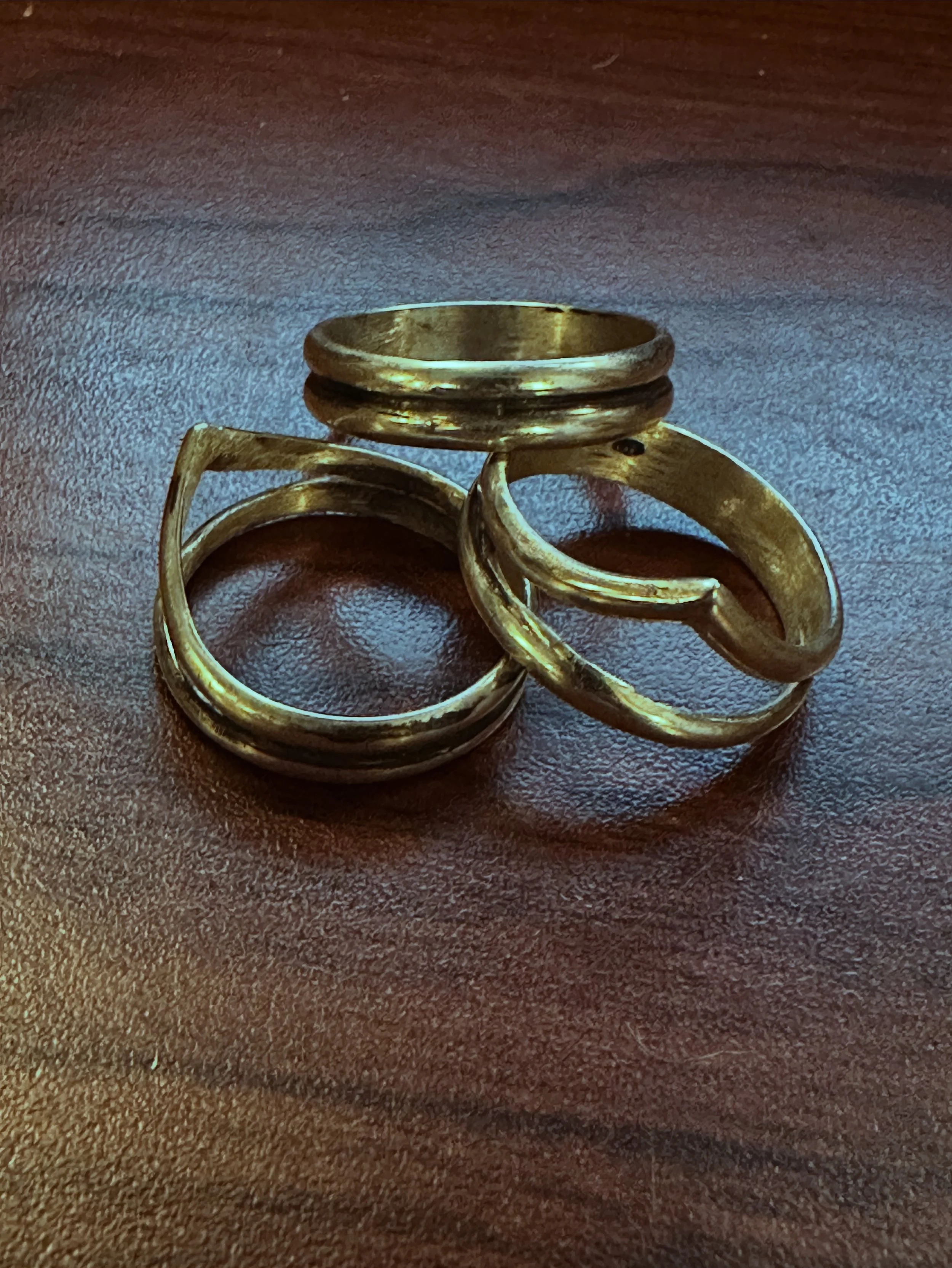 Three Sterling Silver rings resting on a dark wood surface.