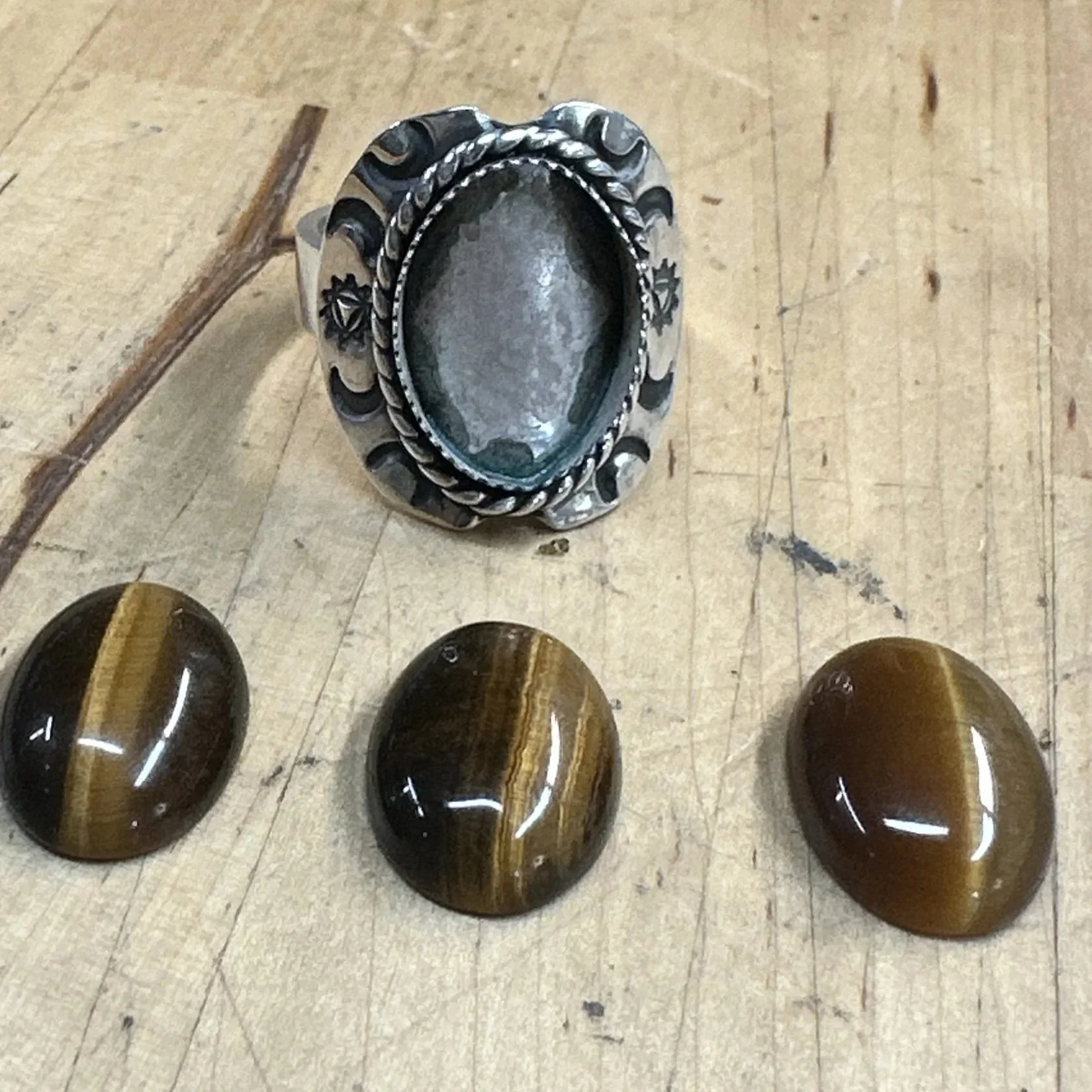 Sterling silver shield ring beside three tiger's eye cabochons