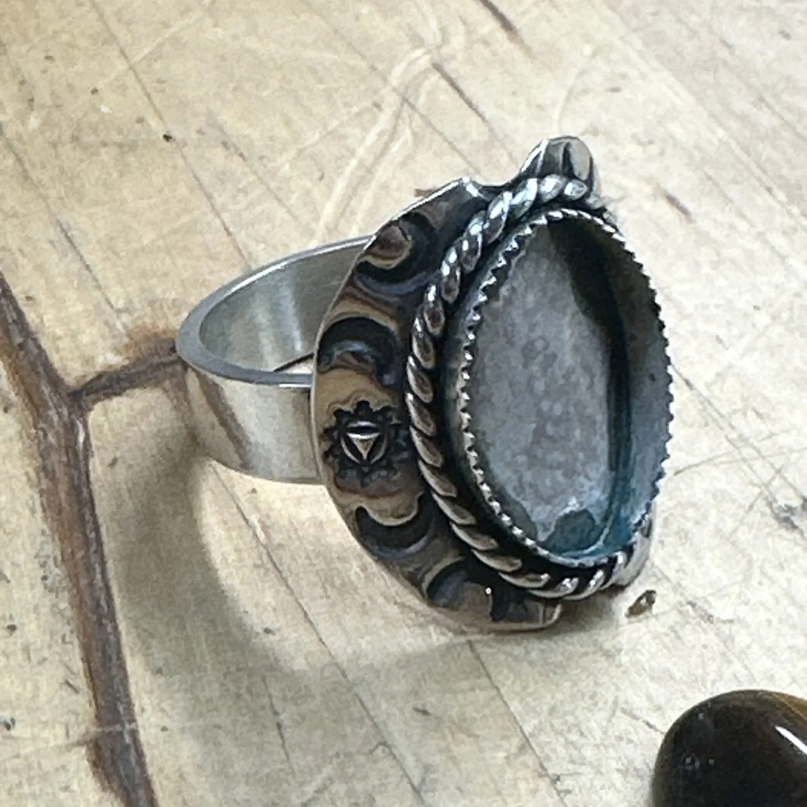 Sterling silver shield ring with an empty rope bezel on a jeweler's bench block