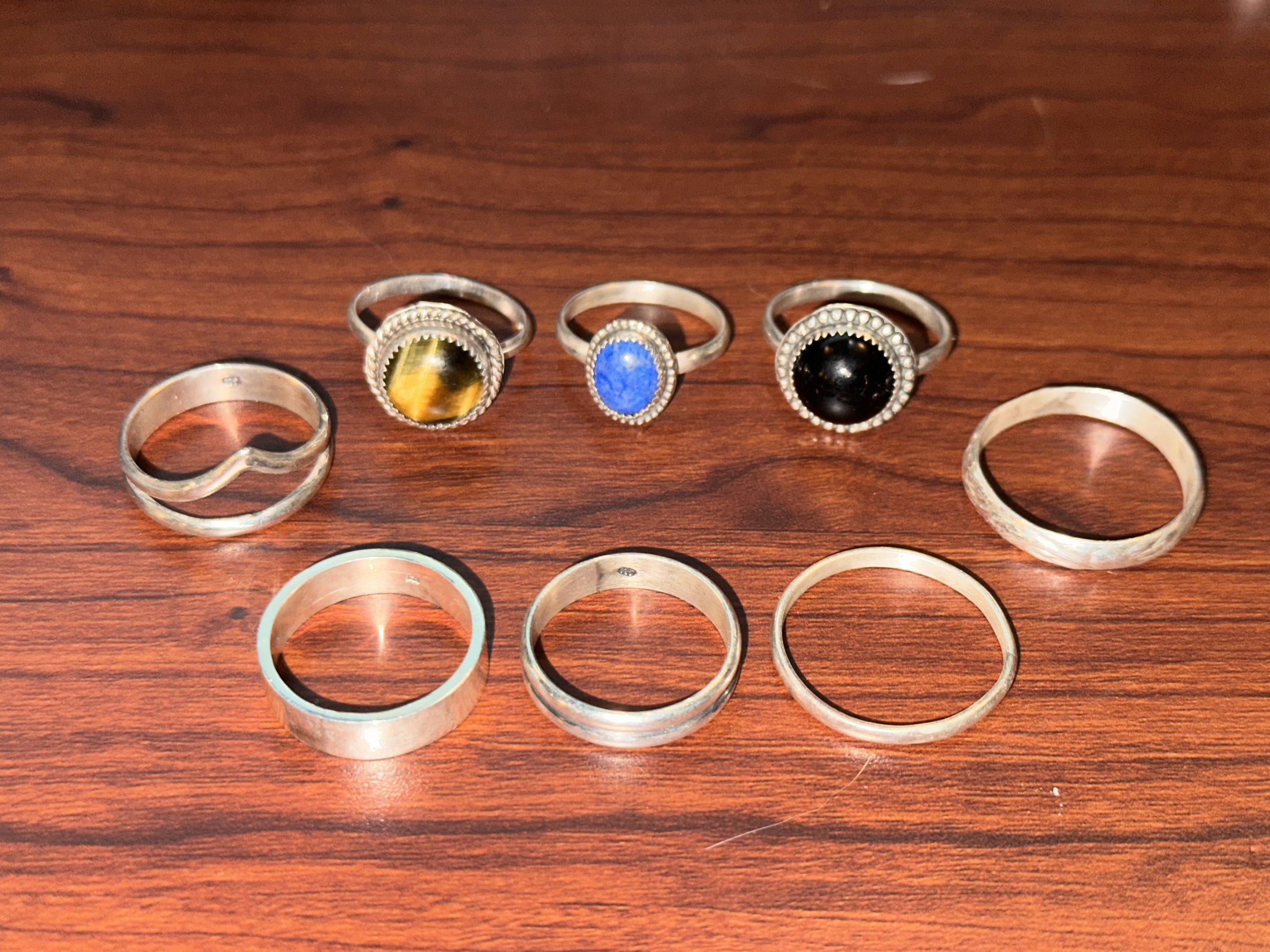 Four rings with various stones and three plain rings on a wooden surface.