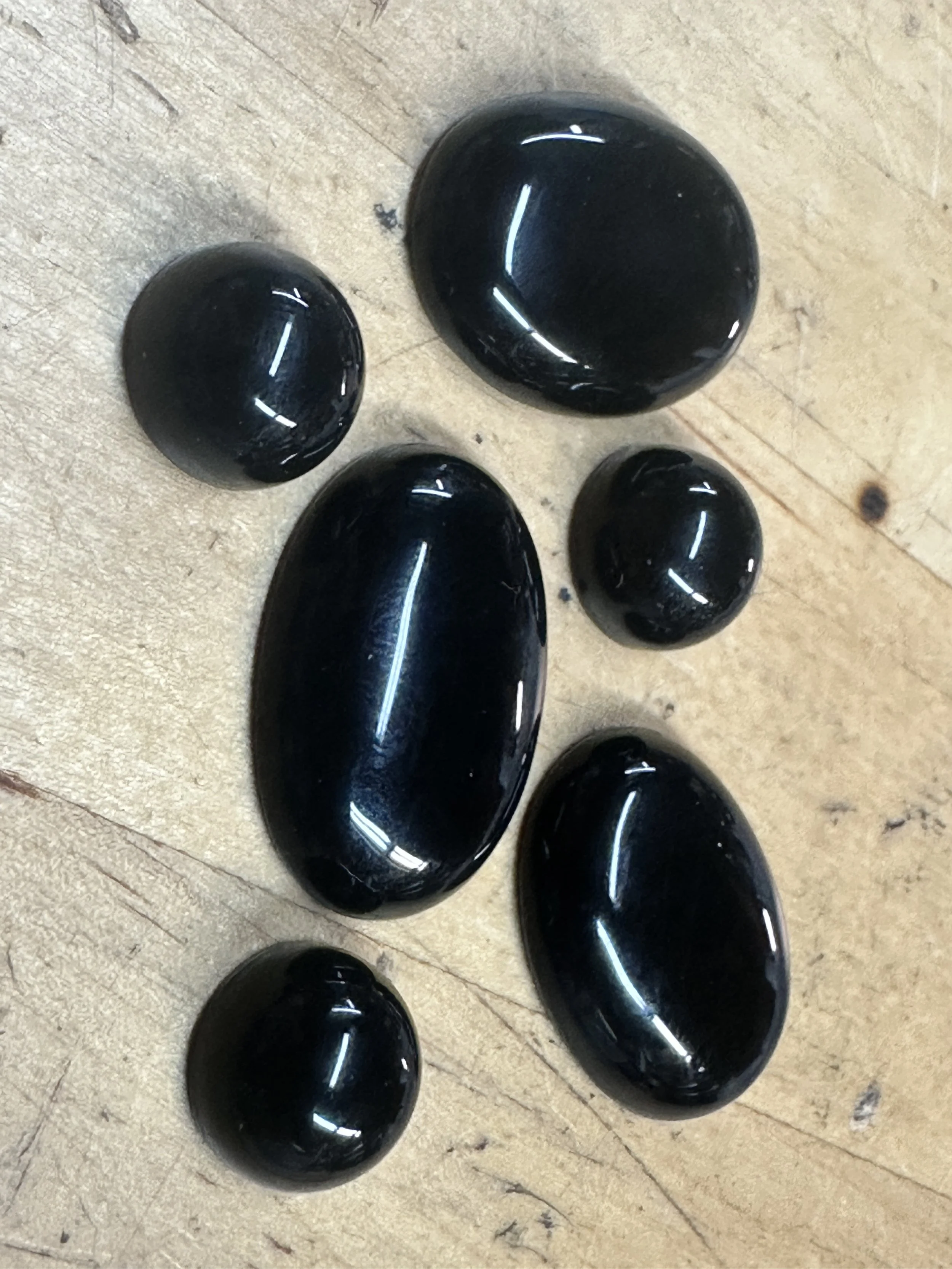 A group of small and large black polished stones or pebbles arranged on a wooden surface.