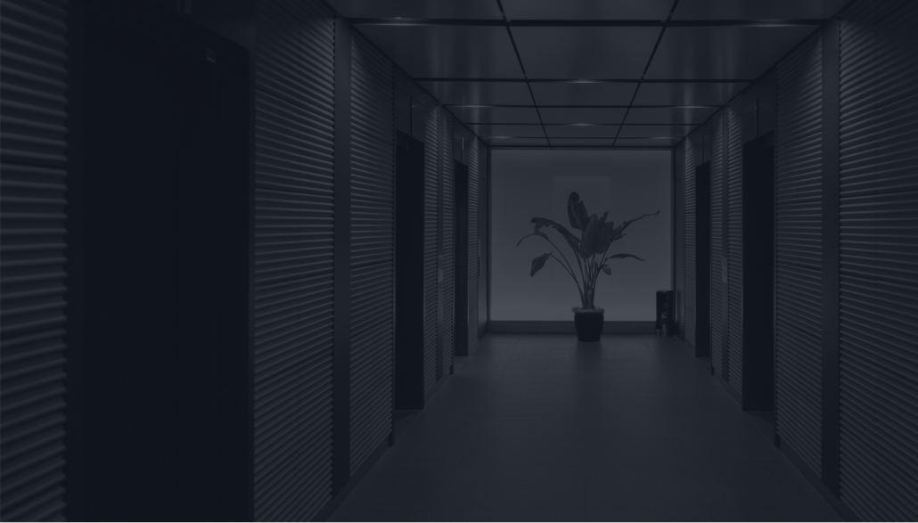 Dimly lit corridor with metal paneled walls and a potted plant at the end of the hallway.