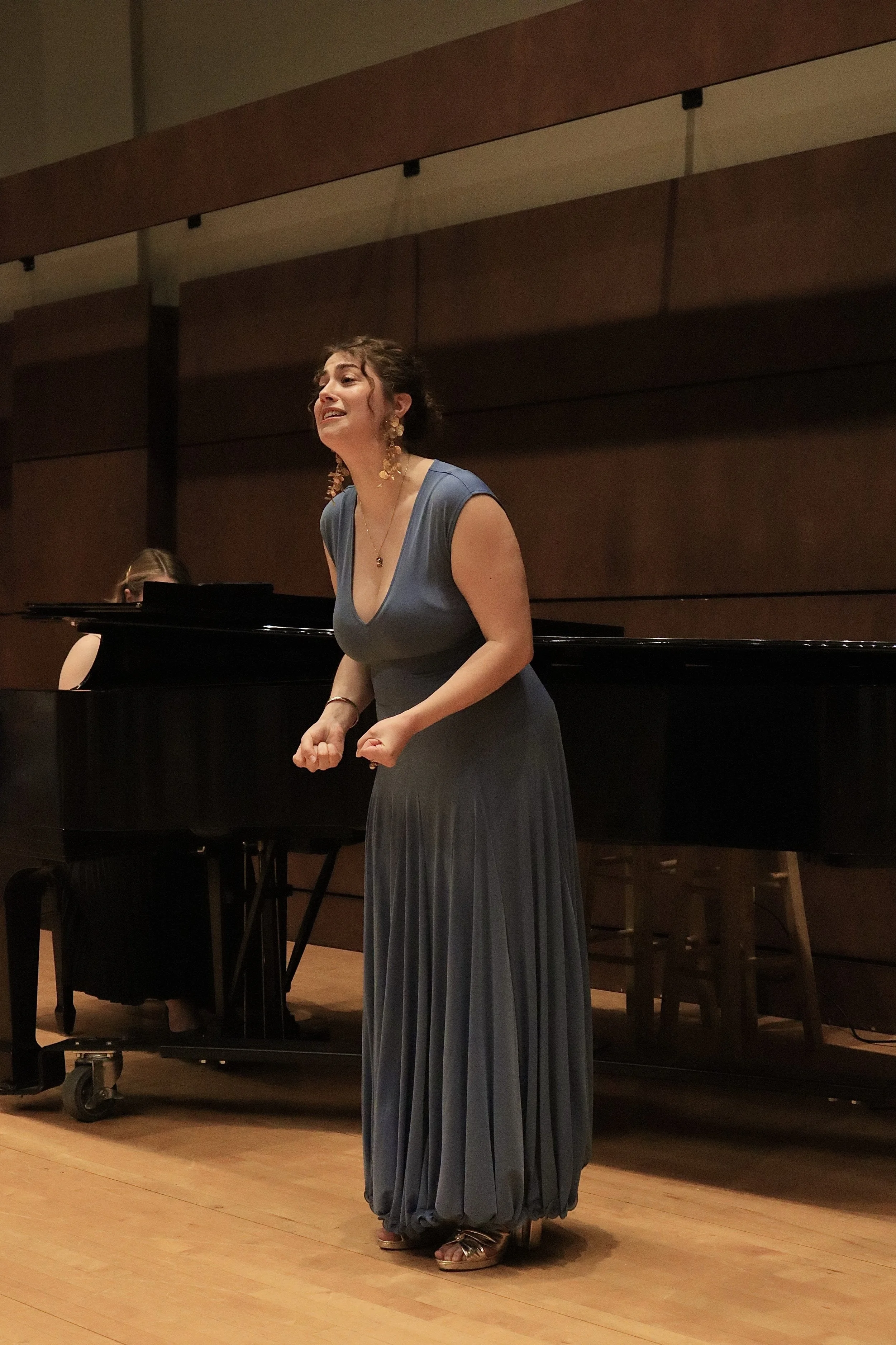 Female singer in a blue gown performing on stage with a pianist in the background.