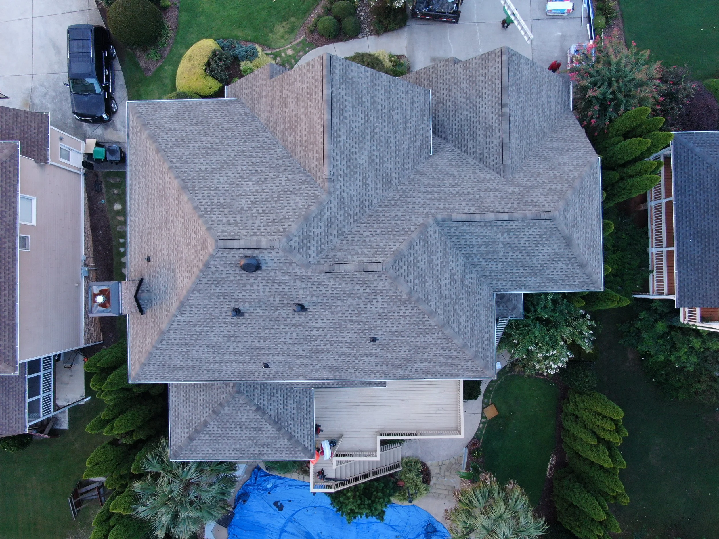 An aerial view of a residential house with a tiled roof, outdoor backyard with greenery, trees, bushes, and a fenced patio.