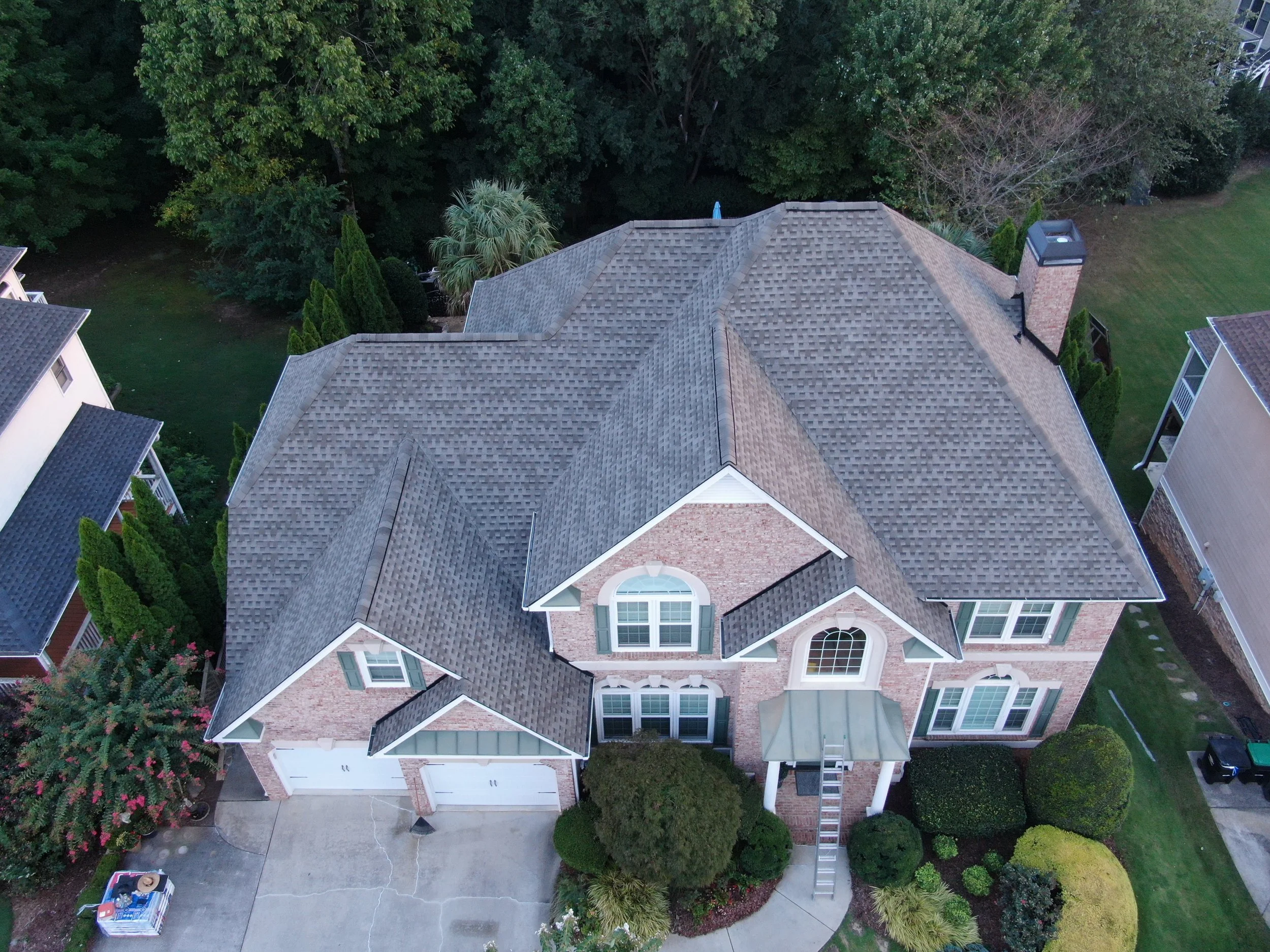Aerial view of a large house with multiple gable roofs, surrounded by trees and a backyard with a lawn and a chimney.