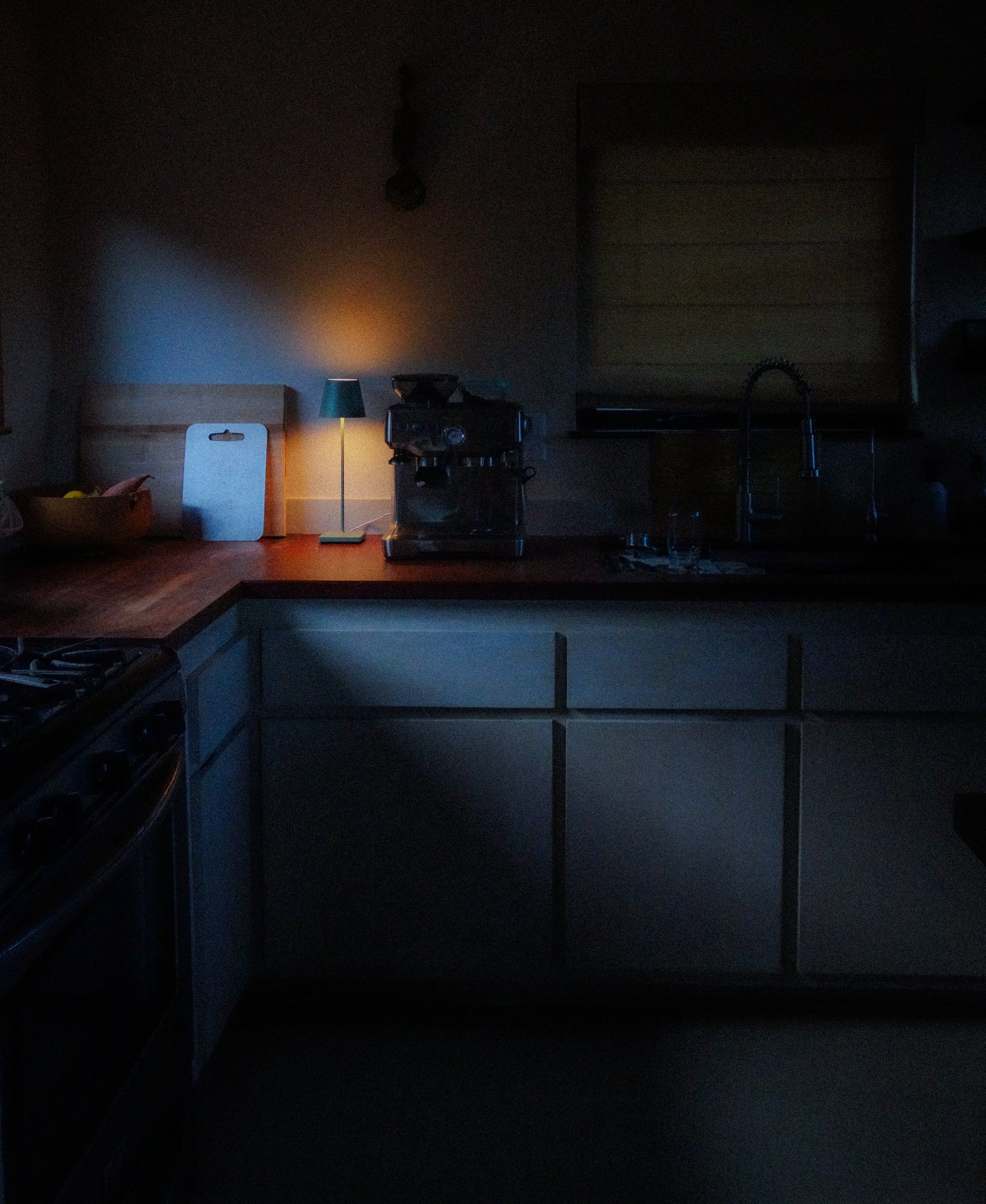 Dark kitchen with dim lighting, a small lamp, and a coffee machine on the countertop.