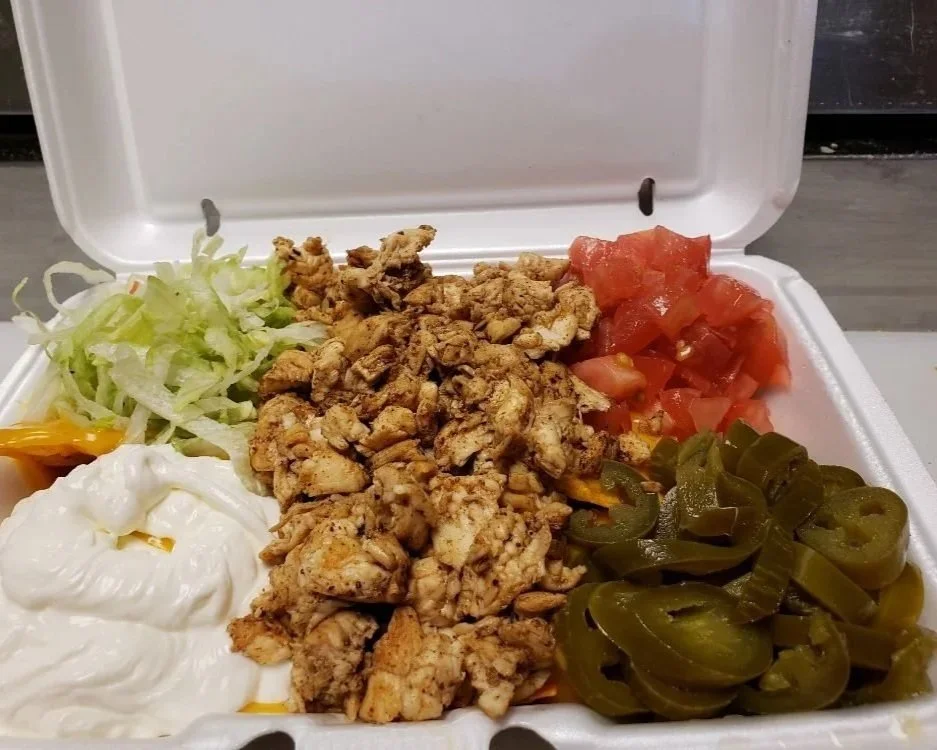 Takeout container with shredded lettuce, cooked chicken, chopped tomatoes, sliced jalapenos, sour cream, and shredded cheese.