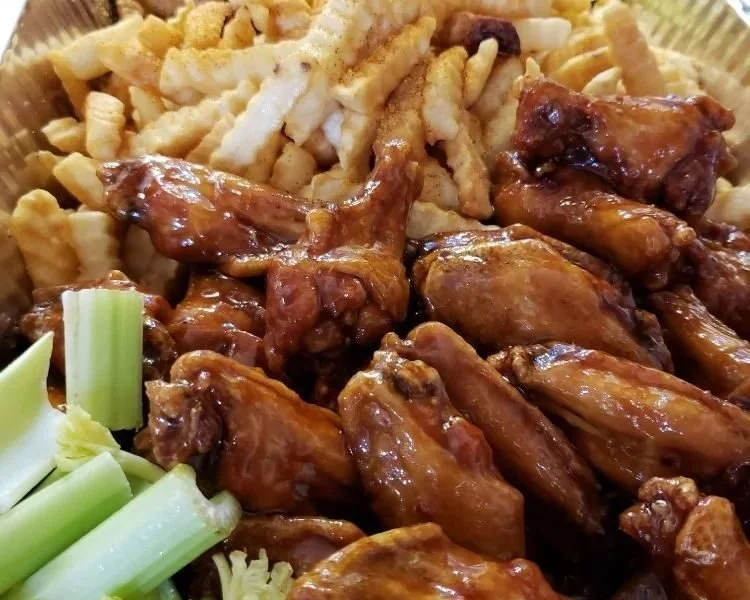 Close-up of barbecue chicken wings with sauce, macaroni and cheese, and celery sticks on a plate.