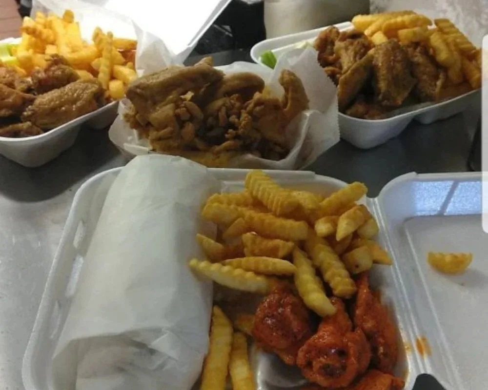 Four takeout containers filled with fried chicken, French fries, and fried fish, on a table.