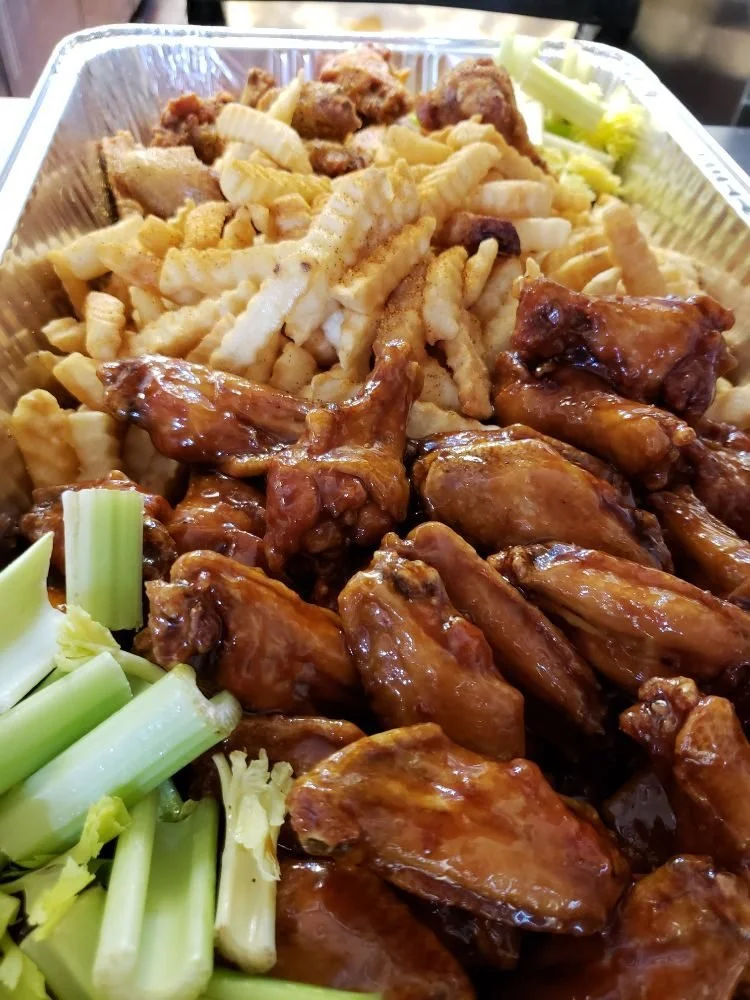 Barbecue chicken wings, French fries with seasoning, celery sticks, and sliced celery in a takeout container.