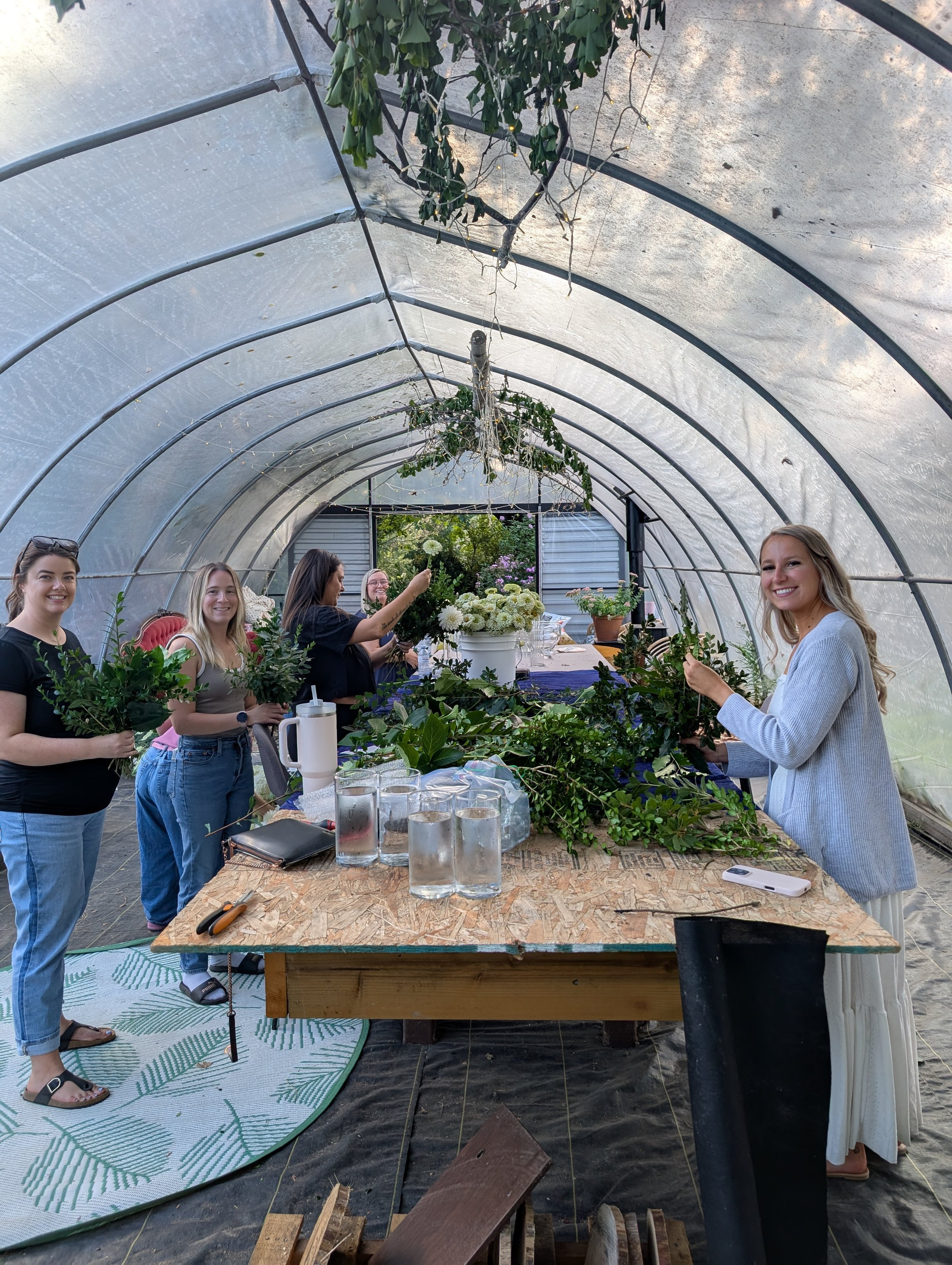 Group of women inside a greenhouse, working with plants and flowers on a wooden table.