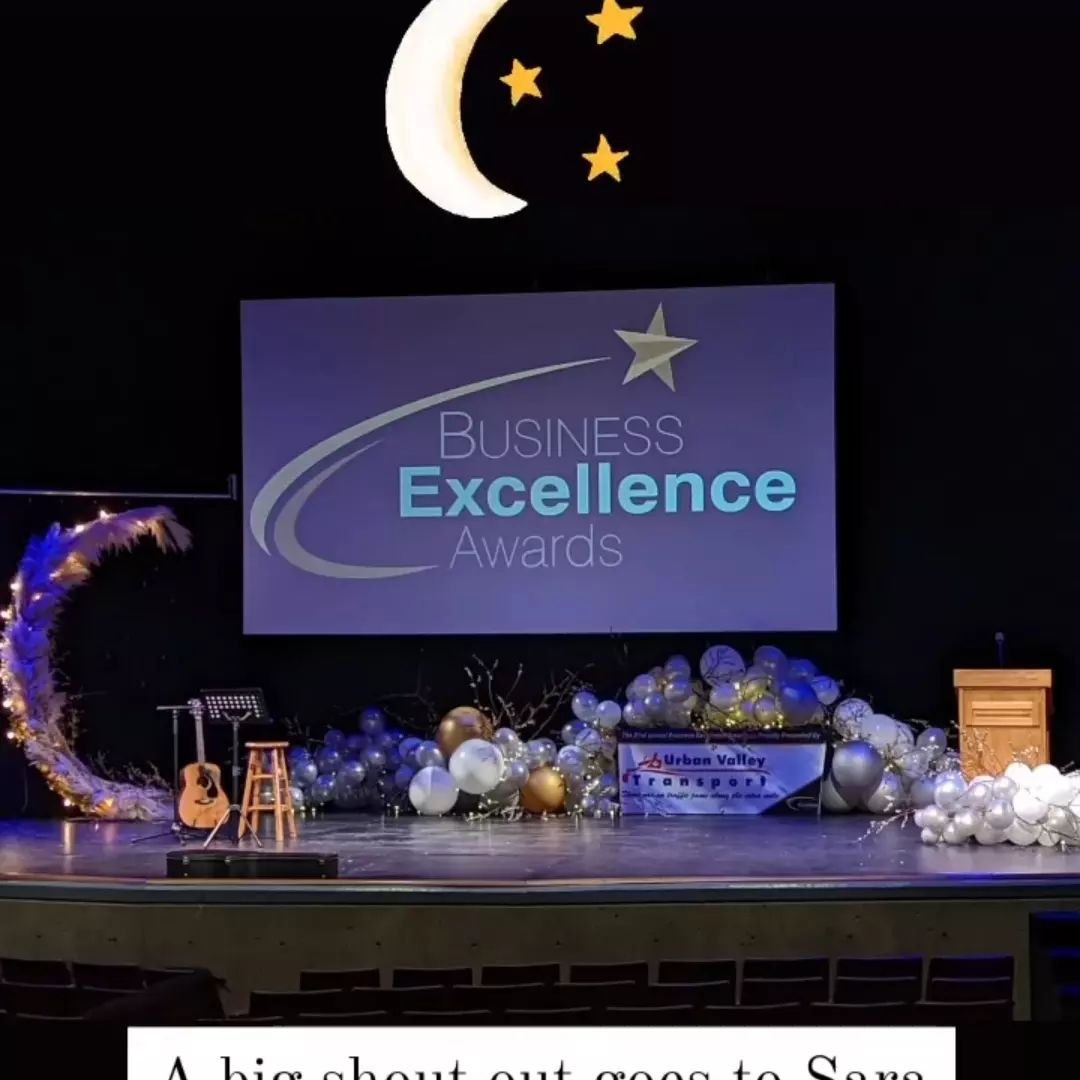 Stage setup for a Business Excellence Awards event with balloons, a moon and star decoration, a podium, and a large screen displaying the event logo.