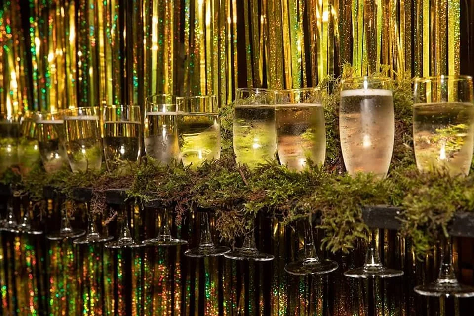 Glasses of champagne on a decorated table with gold and green tinsel background and fir branches.