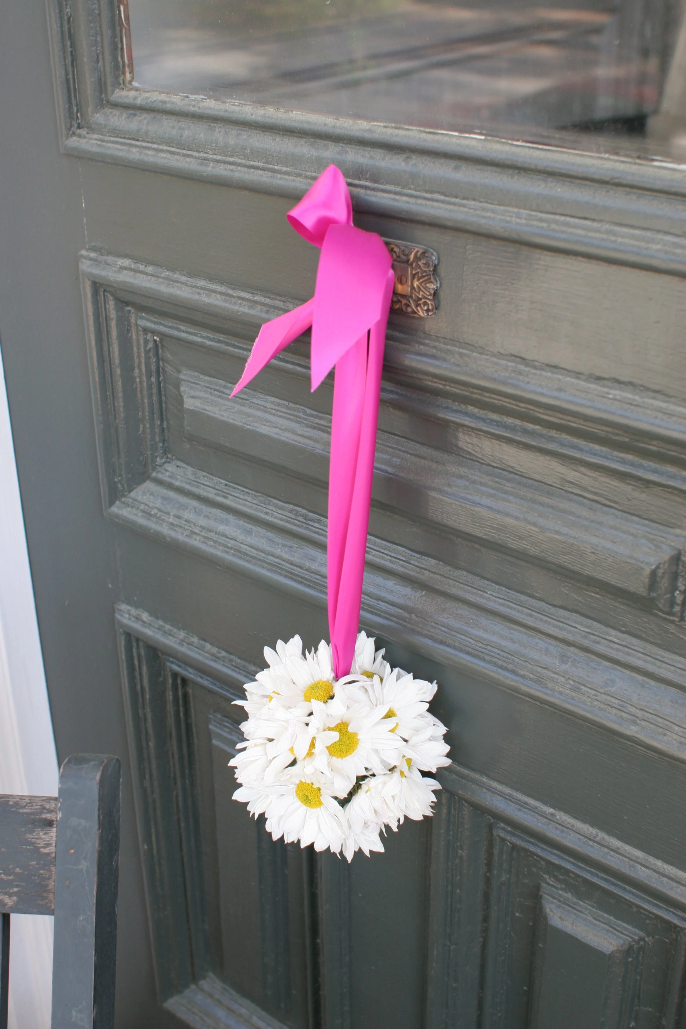 Pink ribbon with a bow attached to a bronze door handle, with a bouquet of white daisies hanging from it.