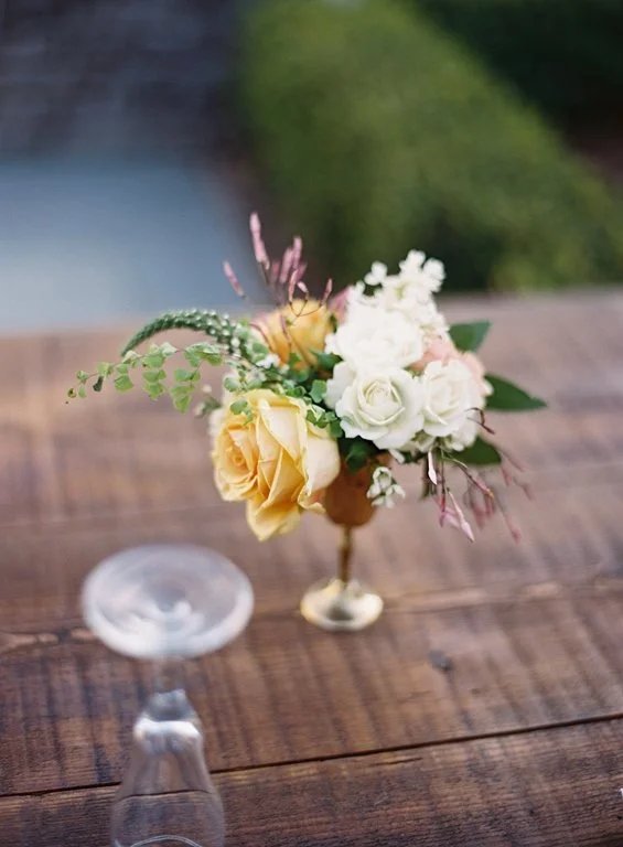Small bouquet of yellow and white roses with greenery on a wooden table
