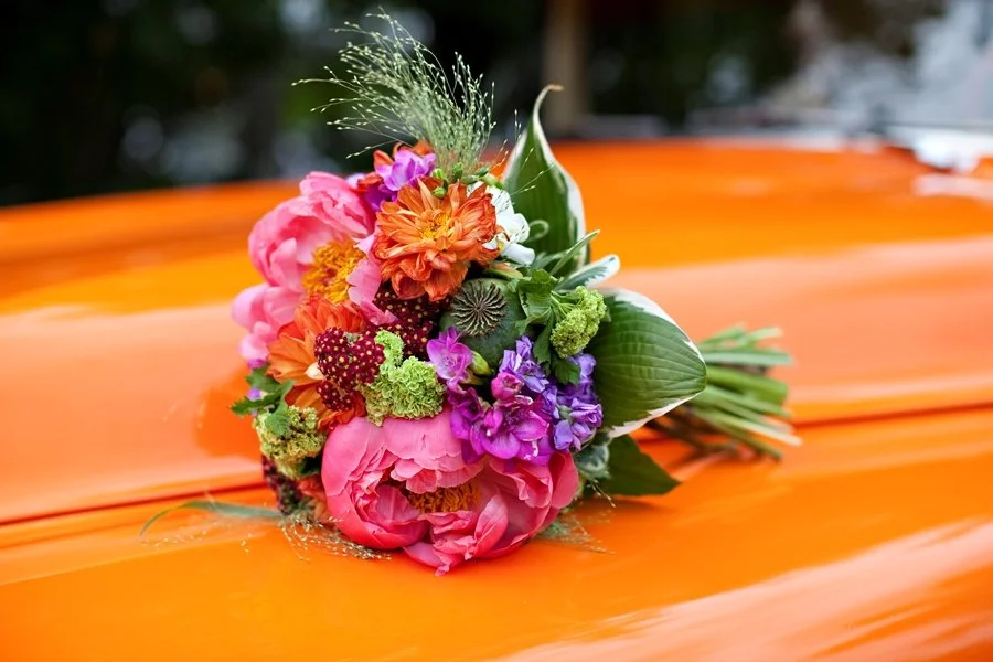 A colorful bouquet of flowers resting on an orange surface, with blurred trees in the background.