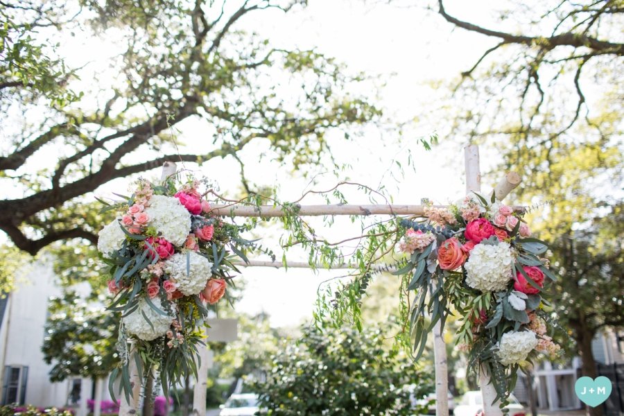 Floral arch decorated with pink and white flowers, greenery, outdoors during daytime.