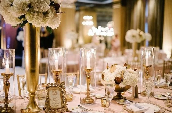Elegant banquet table decorated with white flowers, gold candlesticks, and glassware in a luxurious setting.