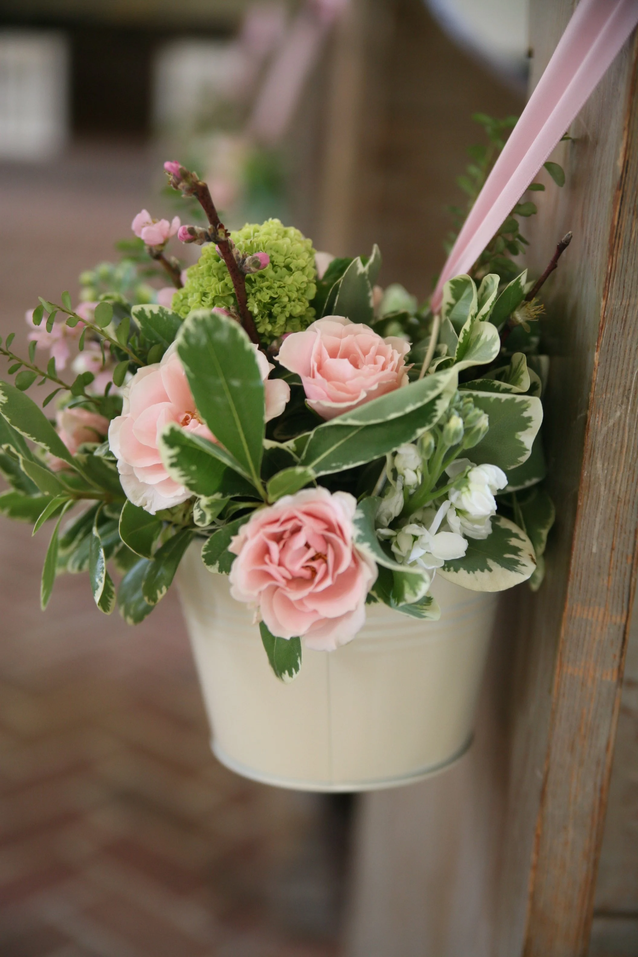 A hanging flower basket with pink roses, white flowers, green leaves, and a green hydrangea, suspended from a wooden structure.
