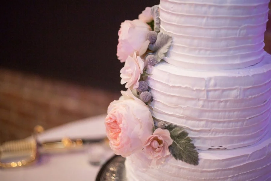 Close-up of a three-tiered white wedding cake decorated with pink and purple flowers and green leaves.