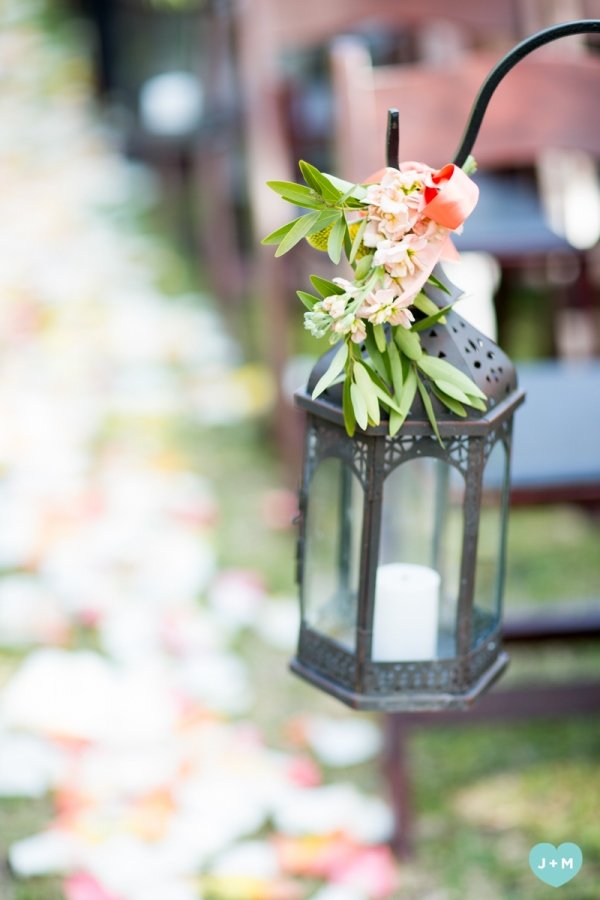 Lantern decorated with pink flowers and green leaves with a candle inside, hanging outdoors.