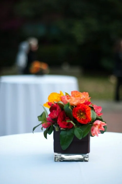 Colorful bouquet of flowers in a black square vase on a white table outdoors