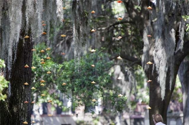 String of small, colorful umbrellas hanging from strings between trees in a park.