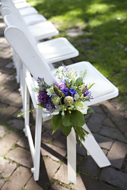 A bouquet of flowers resting on a white folding chair outdoors.