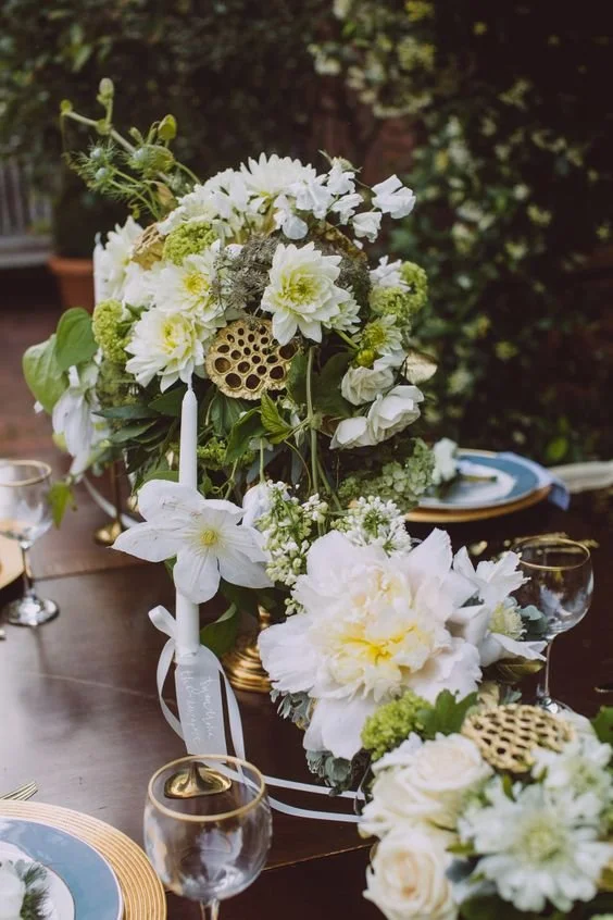 Elegant table centerpiece featuring white flowers, candles, and decorative Lotus seed pods on a wooden table.