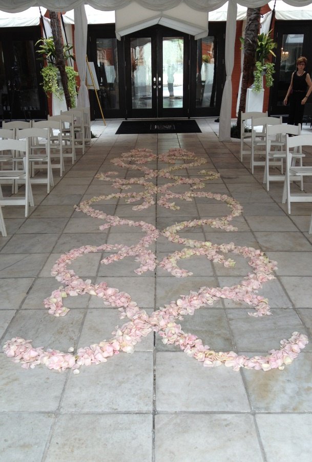 Flower petals arranged on the floor to form a decorative pattern or pathway at an event venue, with seating arranged on either side and a tent overhead.