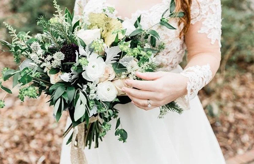 Bride holding a bouquet of white and green flowers outdoors.