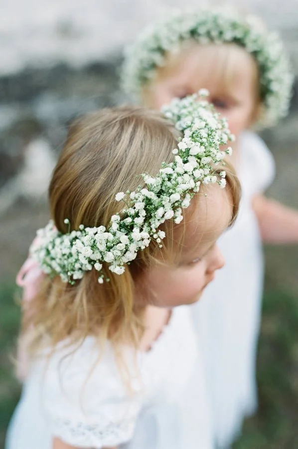 Two young girls wearing flower crowns made of small white flowers during a celebration or outdoor event.