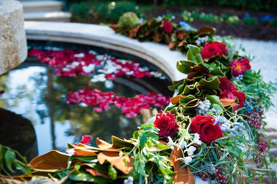 Flower arrangement with roses and greenery by a pond with floating pink flower petals.