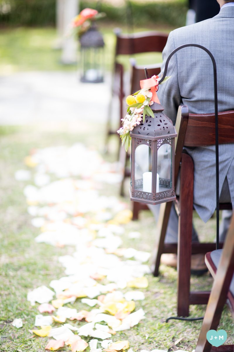 Wedding or outdoor event setup with lanterns attached to chairs and flower petals on the ground