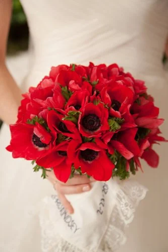 A person in a white dress holding a bouquet of red flowers, including anemone.