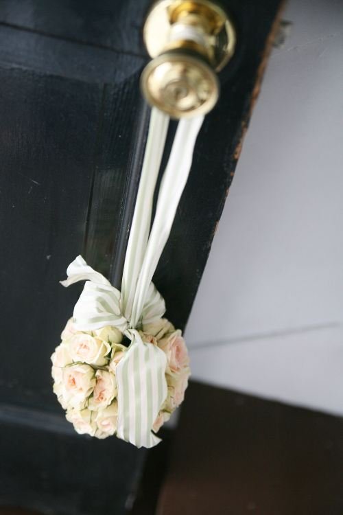 A door with a gold doorknob, a bouquet of pink and white roses tied with a green-and-white striped ribbon hanging from the doorknob.
