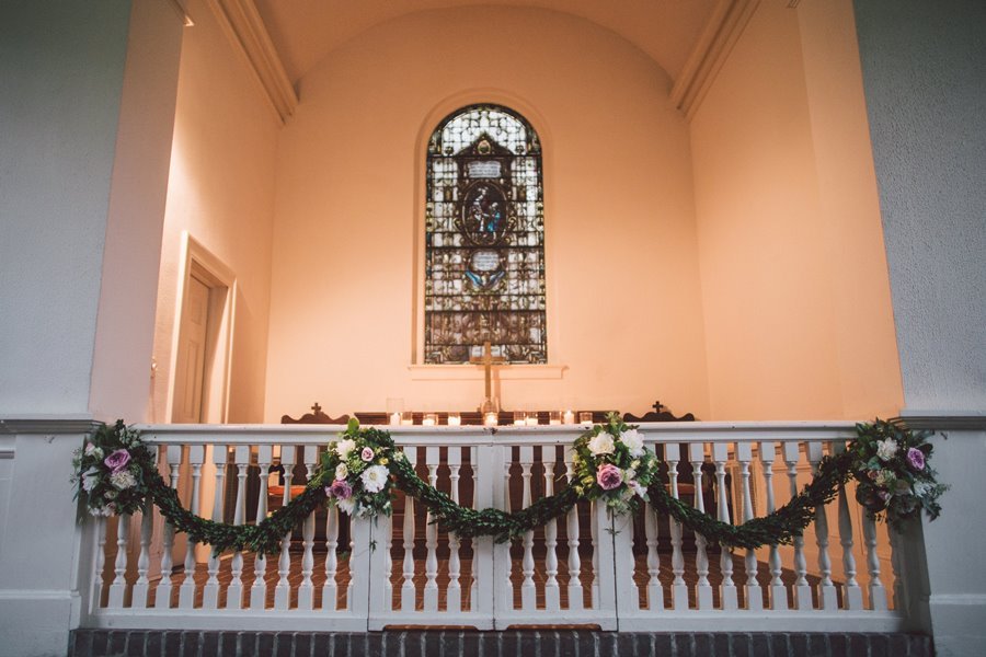 Decorated church altar with floral arrangements and greenery garland in front of a stained glass window.