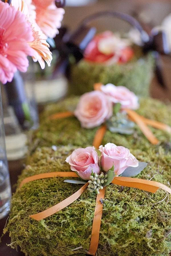 Decorative moss-covered package tied with orange ribbon, adorned with pink roses and green foliage.