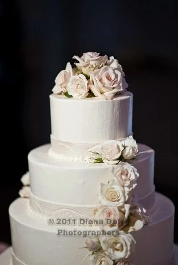 A three-tier white wedding cake decorated with white and blush pink roses.