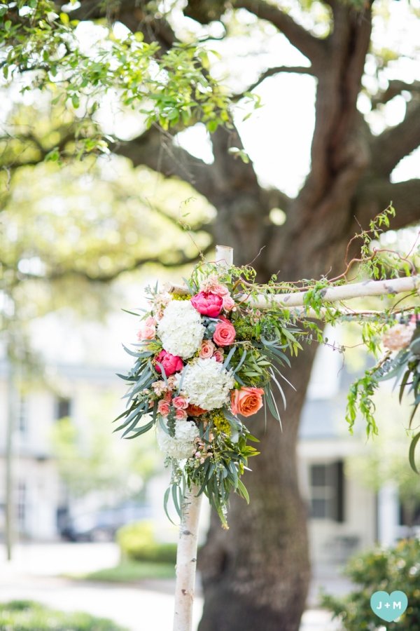 A floral arrangement hanging on a white wooden structure outdoors, with a large tree in the background, during daytime.